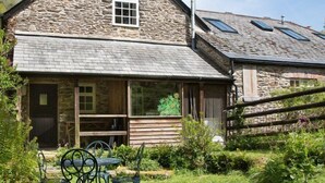 A stone building with a sloped roof, a small window, and a chimney. There is a wooden deck with a table and chairs outside. - Watermill Cottages (Dartmouth)