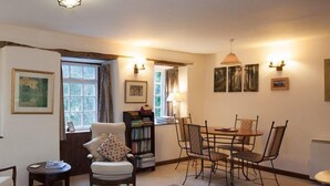 A cozy living room with a fireplace, a dining area with a table and chairs, and a bookshelf filled with books. - Watermill Cottages (Dartmouth)
