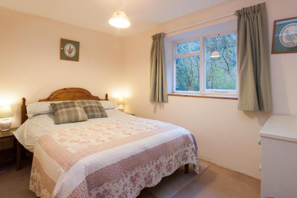 A bedroom with a bed, bedside lamps, a window with curtains, and a wall-mounted picture.