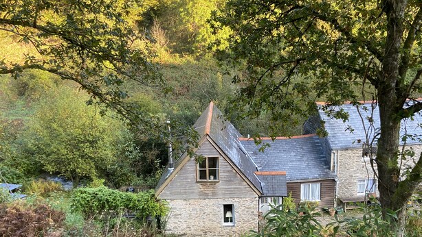 A rustic stone house with a sloped roof, surrounded by dense greenery and trees. - Watermill Cottages (Dartmouth)