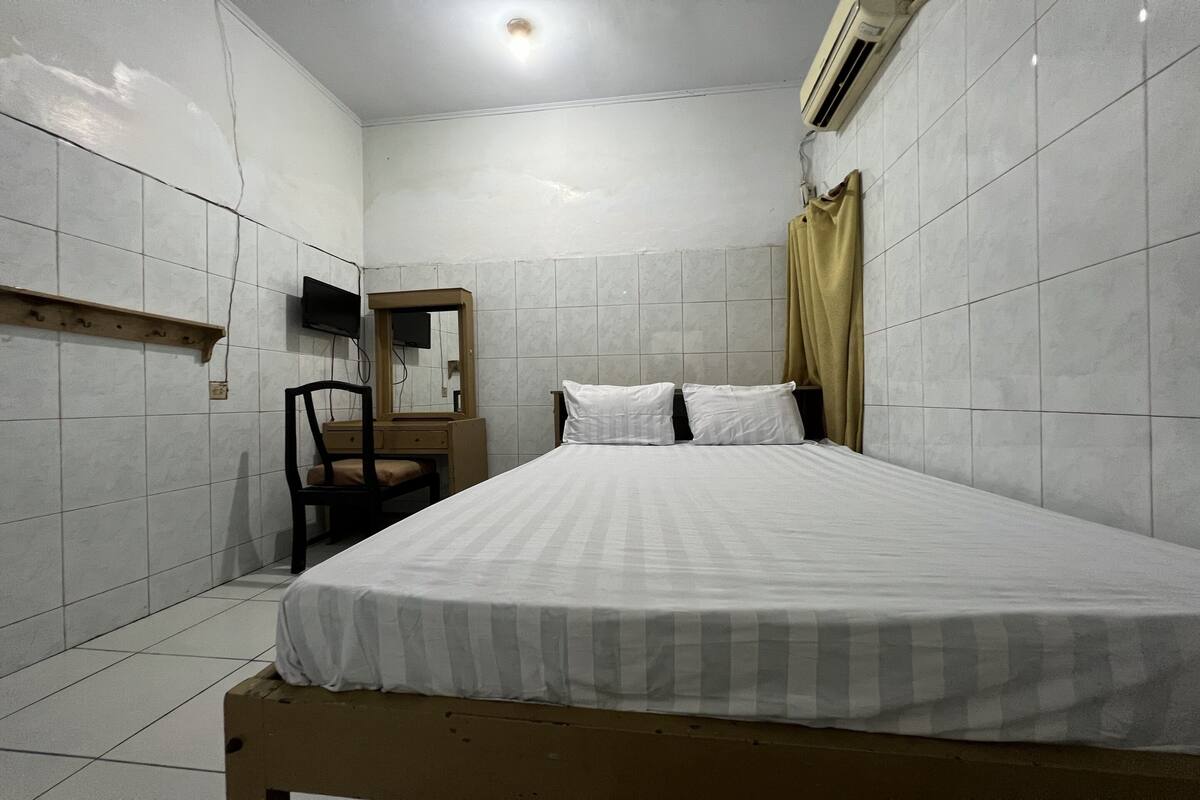 A bedroom with a bed, a chair, a wooden shelf, a television, and a mirror.