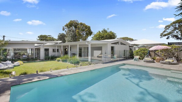 A modern house with a swimming pool, covered outdoor seating, and a well-maintained garden. - Heated swimming pool and walk to beach (BATEAU BAY)