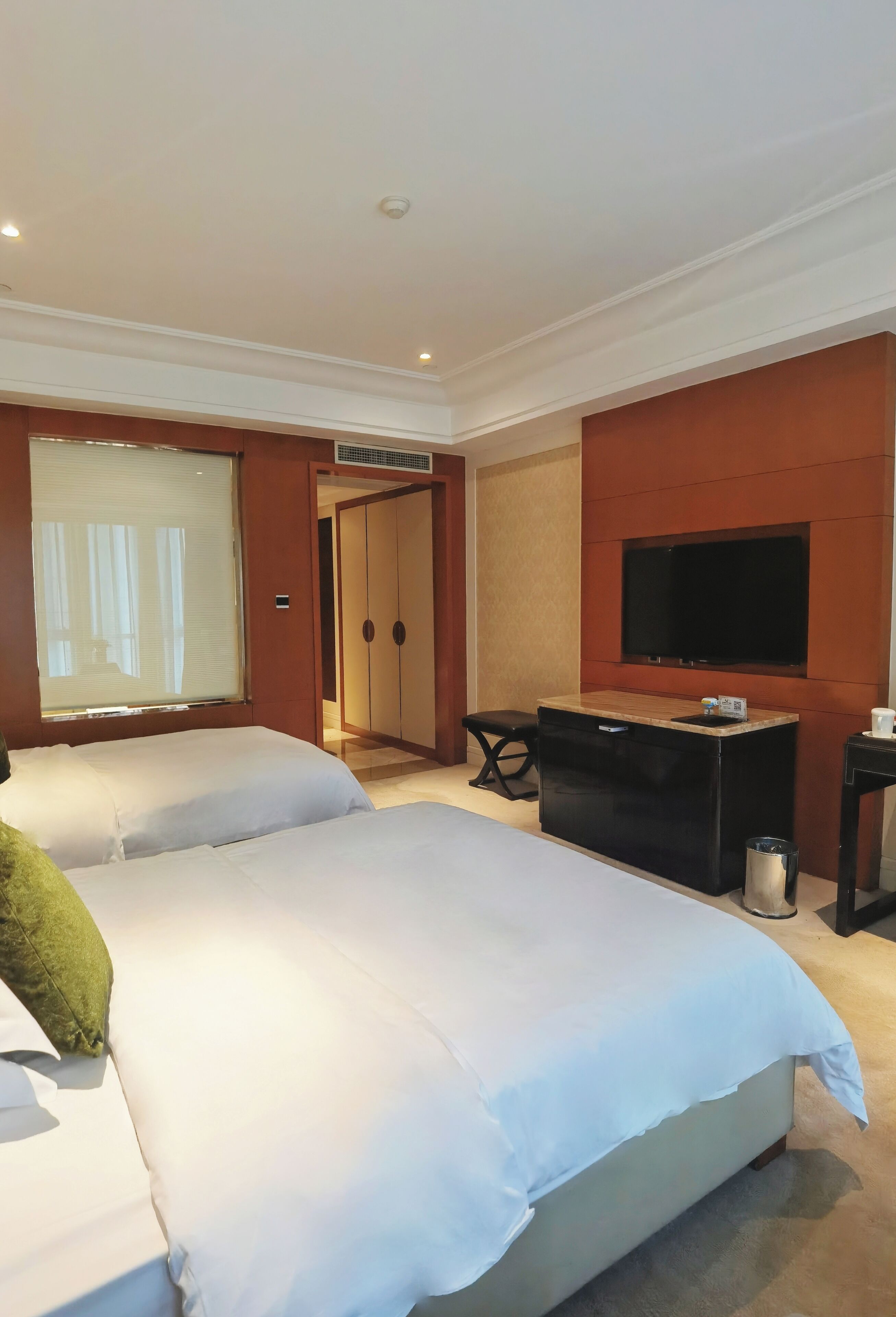 A hotel room with a large bed, a television mounted on the wall, a desk with a chair, and a wardrobe.