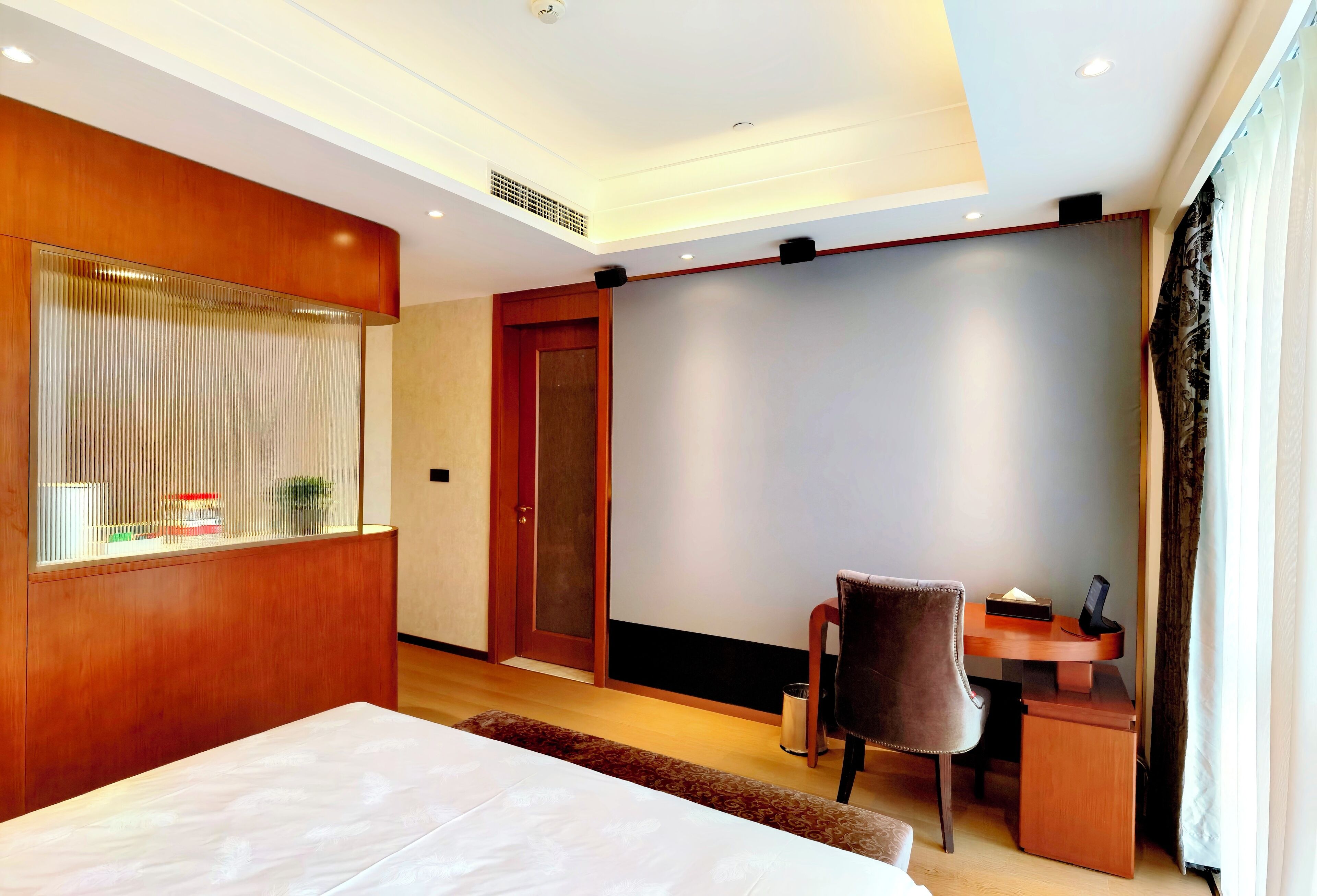 Une chambre d’hôtel avec un grand lit, un bureau avec une chaise, une cloison en bois et une grande fenêtre avec des rideaux.