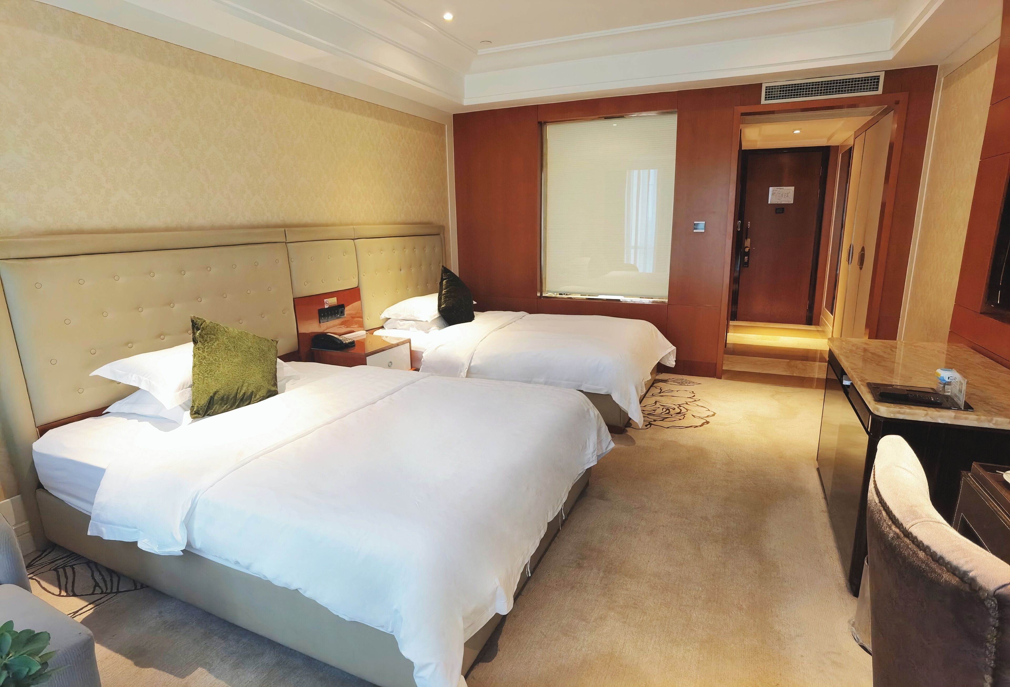 Une chambre d’hôtel avec deux lits, un bureau, une chaise, une grande fenêtre et une porte.