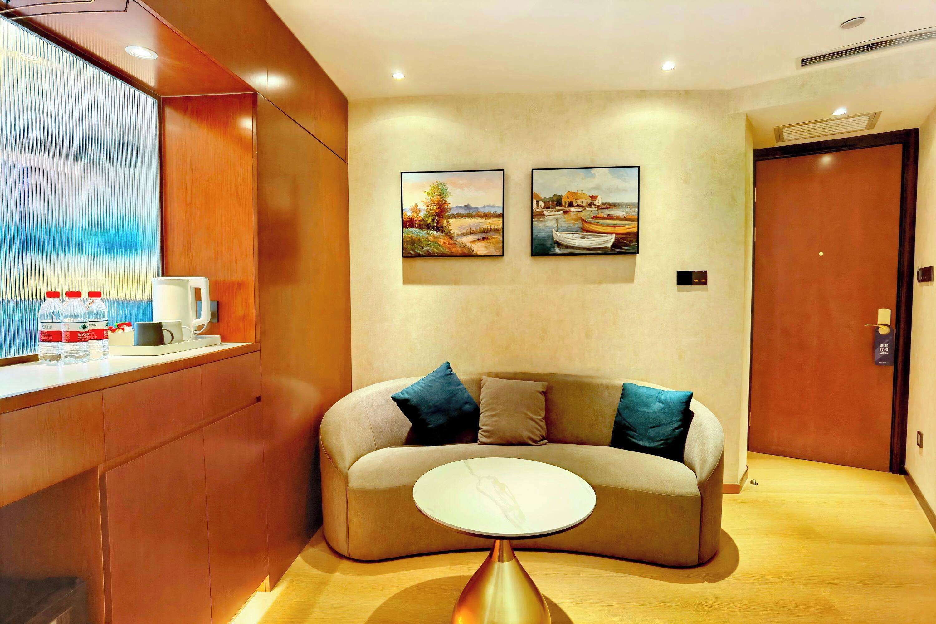 Eine moderne Hotelhalle mit einem Holzbüro, einem beige farbenen Sofa mit blauen Kissen und zwei Landschaftsbildern an der Wand.