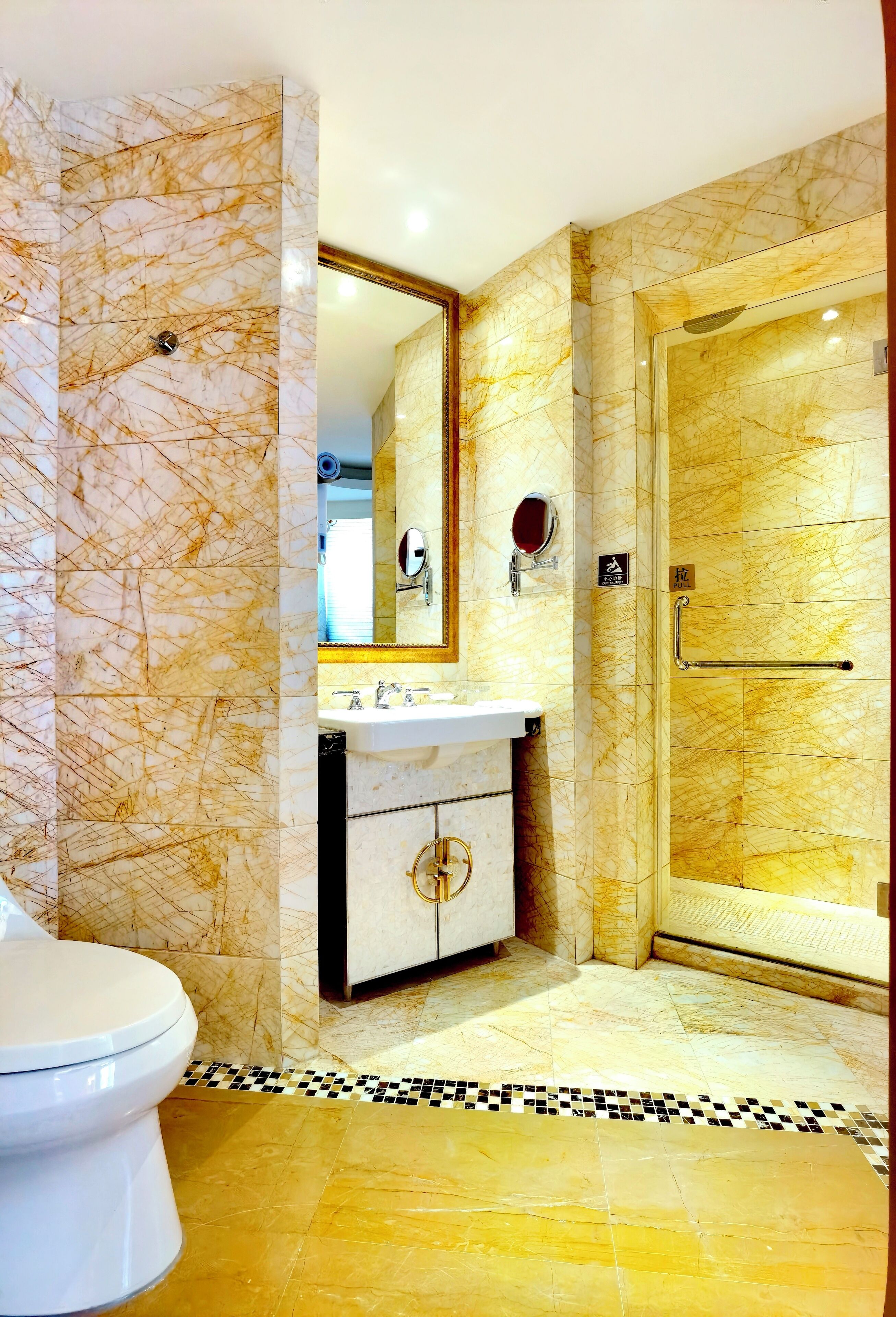 A bathroom with a marble wall, a sink, a toilet, and a shower area.