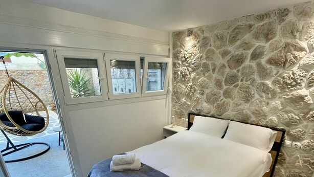 A bedroom with a bed, a hanging chair, and a stone wall. - Central Studio Flat with Garden (Volos)