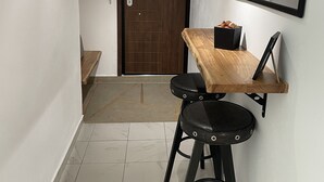 A small, modern room with a wooden dining table and two black bar stools, a wooden door, a mirror, and a light fixture on the ceiling. - Central Studio Flat with Garden (Volos)
