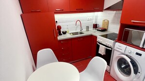 A compact kitchen with red cabinets, a white sink, a microwave, and a washing machine. - Central Studio Flat with Garden (Volos)