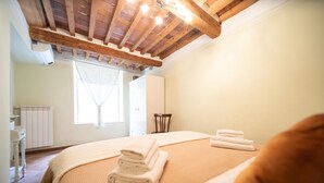 A bedroom with a wooden ceiling, a bed with folded towels, a chair, and a window with curtains. - Madalina Apartment in Center Town (Lucca)