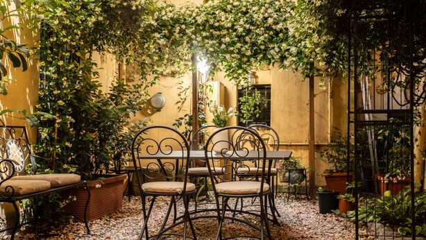 An outdoor patio with a table and chairs, surrounded by potted plants and a yellow wall. - Madalina Apartment in Center Town (Lucca)