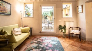 A cozy living room with a sofa, a chair, a floral rug, and a view of the outside through a glass door. - Madalina Apartment in Center Town (Lucca)