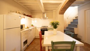 A compact kitchen with white appliances, a dining table, and a staircase leading to another level. - Madalina Apartment in Center Town (Lucca)