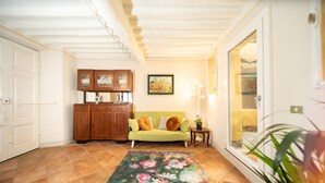 A living room with a green sofa, a floral rug, wooden cabinets, and a painting on the wall. - Madalina Apartment in Center Town (Lucca)