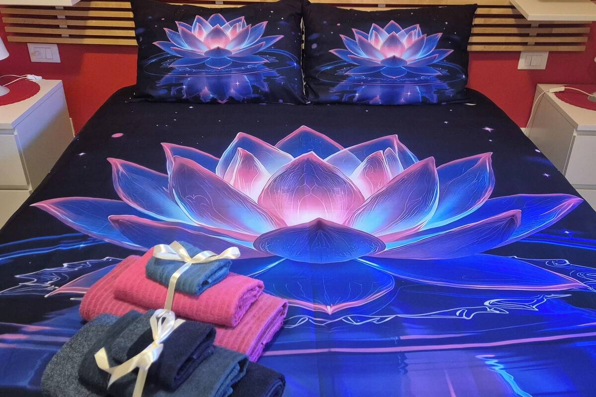 A bed with a lotus-themed bedspread, two bedside tables with lamps, and a red wall.