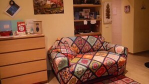 A cozy living room with a colorful quilted sofa, a dining area with a red tablecloth, and a kitchen with white cabinets and a refrigerator. - Lady D. Bed&breakfast  (Rome)