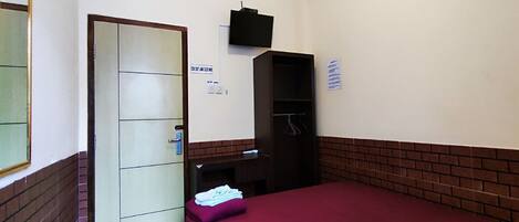 A hotel room with a bed, a wardrobe, a television, and a door.