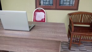 A wooden desk with a laptop, a red chair, and a window with bars. - Hotel O Aksana Homestay SyariahNearWonderland Trik Art (Purwokerto)