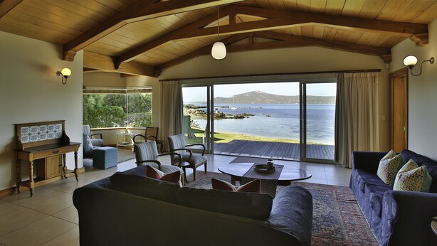 A spacious living area with a large window overlooking a scenic coastal view, wooden ceiling beams, and a cozy seating arrangement. - Sandbaai Villa Langebaan 7 sleeper (Langebaan)