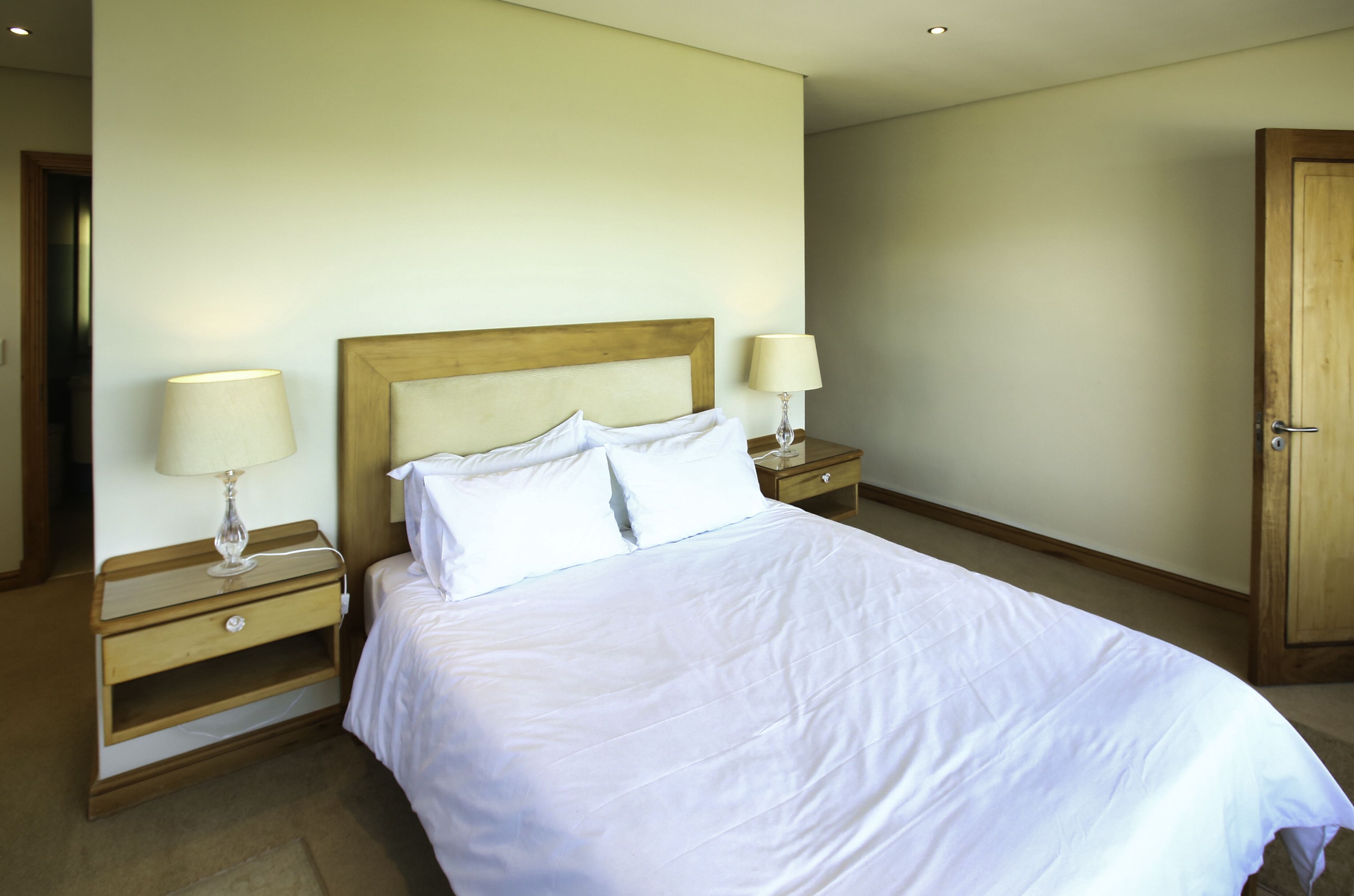 A neatly made bed with white linens, two bedside tables with lamps, and a wooden door.