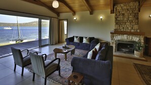 A spacious living room with a stone fireplace, a large sofa, and a view of the sea through a sliding glass door. - Sandbaai Villa Langebaan 7 sleeper (Langebaan)