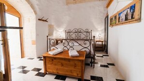 Quarto com uma cama, um baú de madeira, uma mesinha e um quadro na parede.