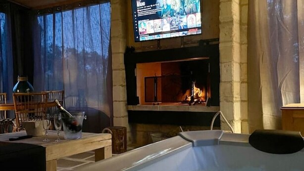 Um quarto com lareira, televisão montada acima dela e uma banheira de hidromassagem em primeiro plano.