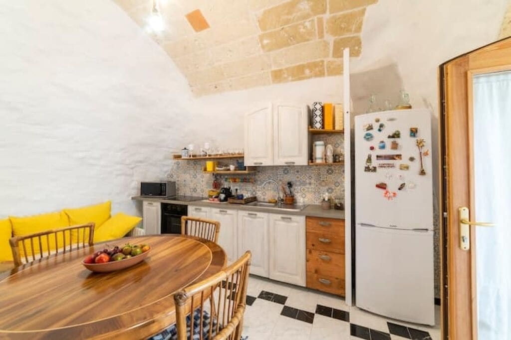 Eine Küche mit weißen Schränken, einem Holzespeisetisch mit Stühlen, einem Kühlschrank und einer gefliesten Spritzschutzleiste.