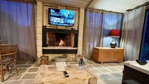 Uma sala de estar aconchegante com lareira, uma televisão montada acima e uma mesa de centro de madeira, além de uma cadeira de vime.