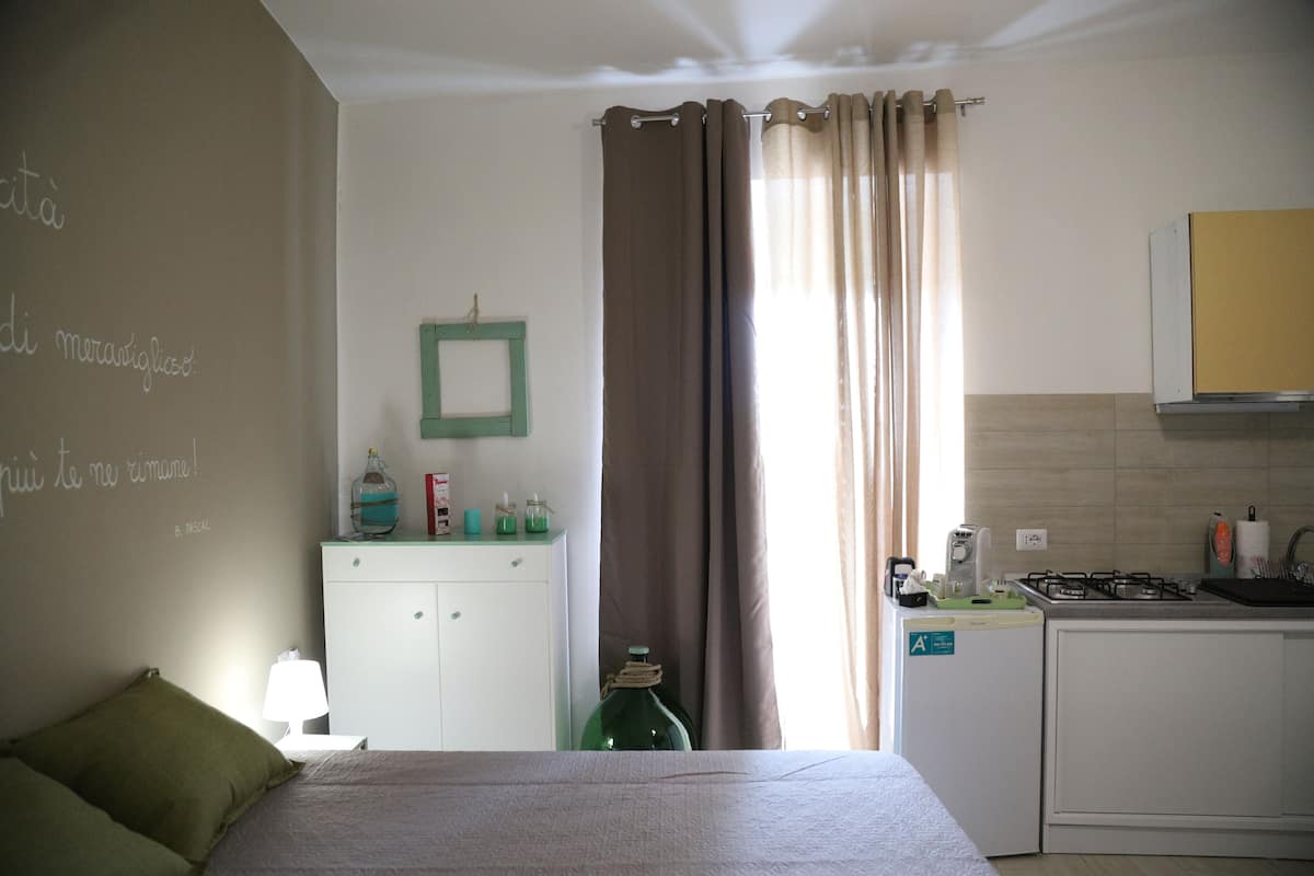 A bedroom with a bed, a nightstand, a dresser, and a kitchenette.