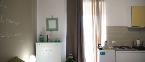 A bedroom with a bed, a nightstand, a dresser, and a kitchenette.