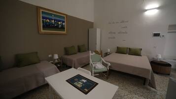 Una camera d'albergo con due letti singoli, un divano, un tavolo e un quadro appeso al muro.