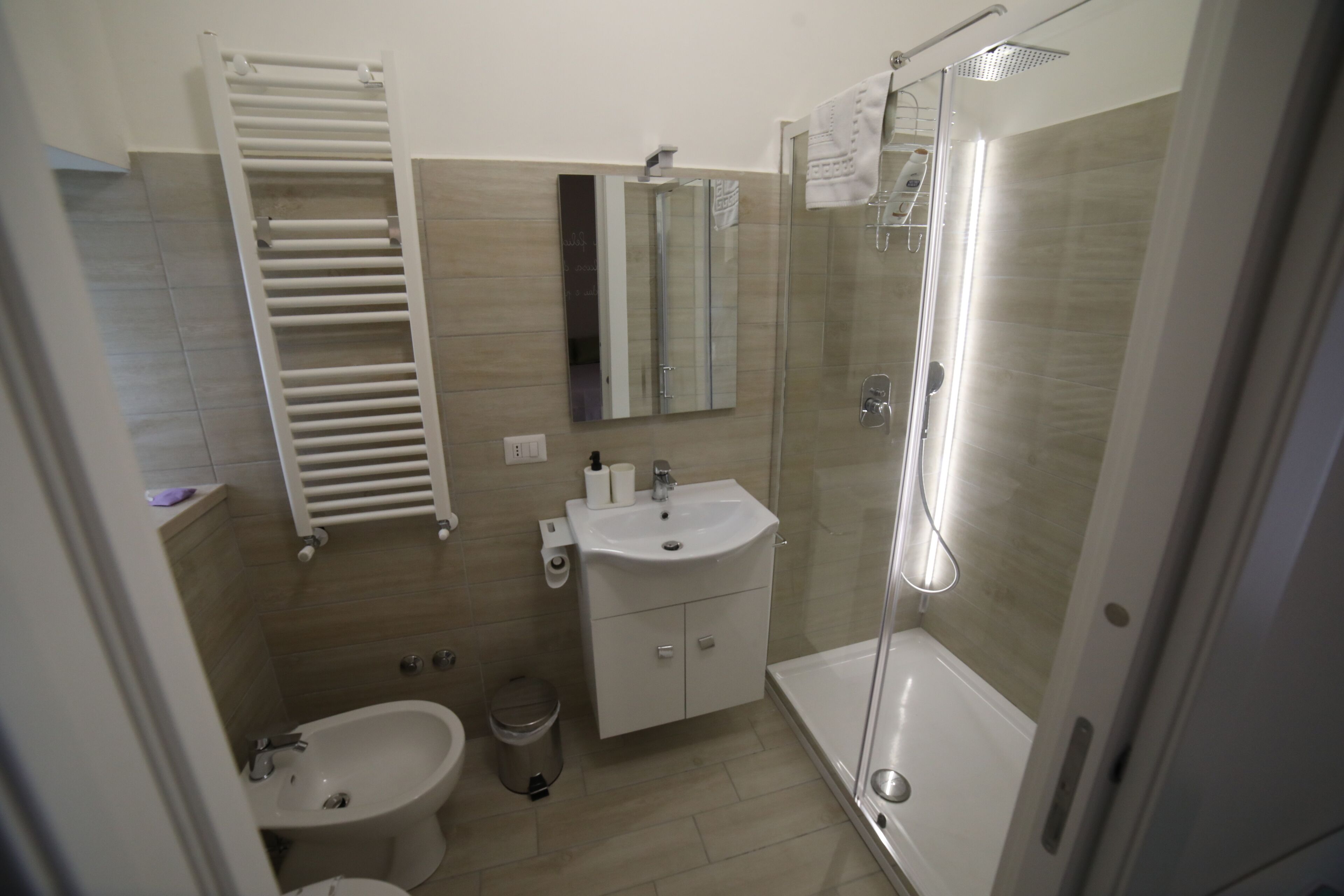 Un baño moderno con inodoro, bidé, lavamanos, espejo y ducha con cerramiento de vidrio.