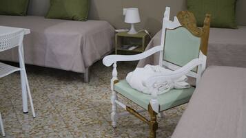 A hotel room with a bed, a chair with a towel, a small table, and a nightstand with a lamp.