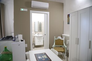 A compact hotel room with a kitchenette, a small bathroom, a dining area, and a wardrobe.