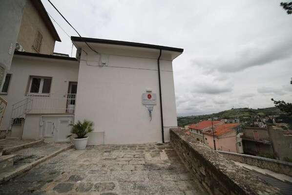 A building with a stone staircase leading to a white door, a potted plant, and a view of a town with red-roofed buildings.