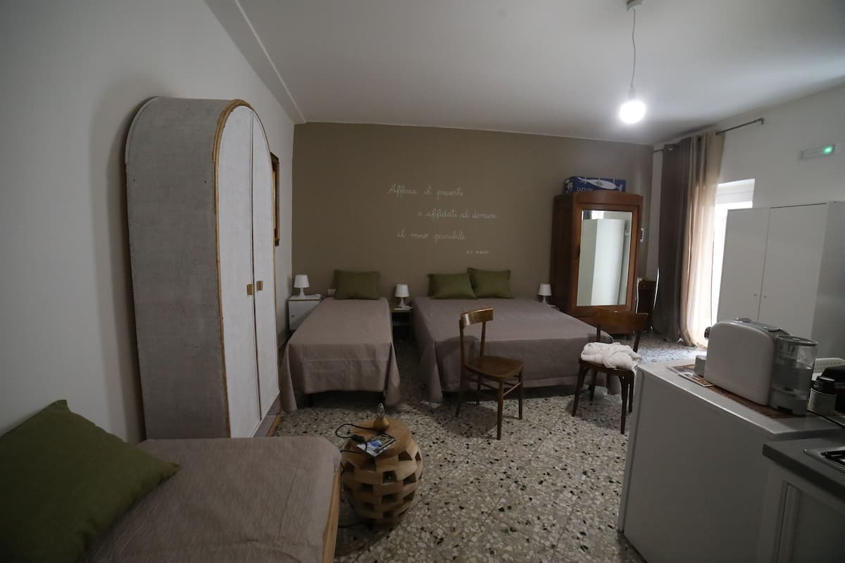 A hotel room with two single beds, a small kitchenette, a mirror, and a wall with a quote.