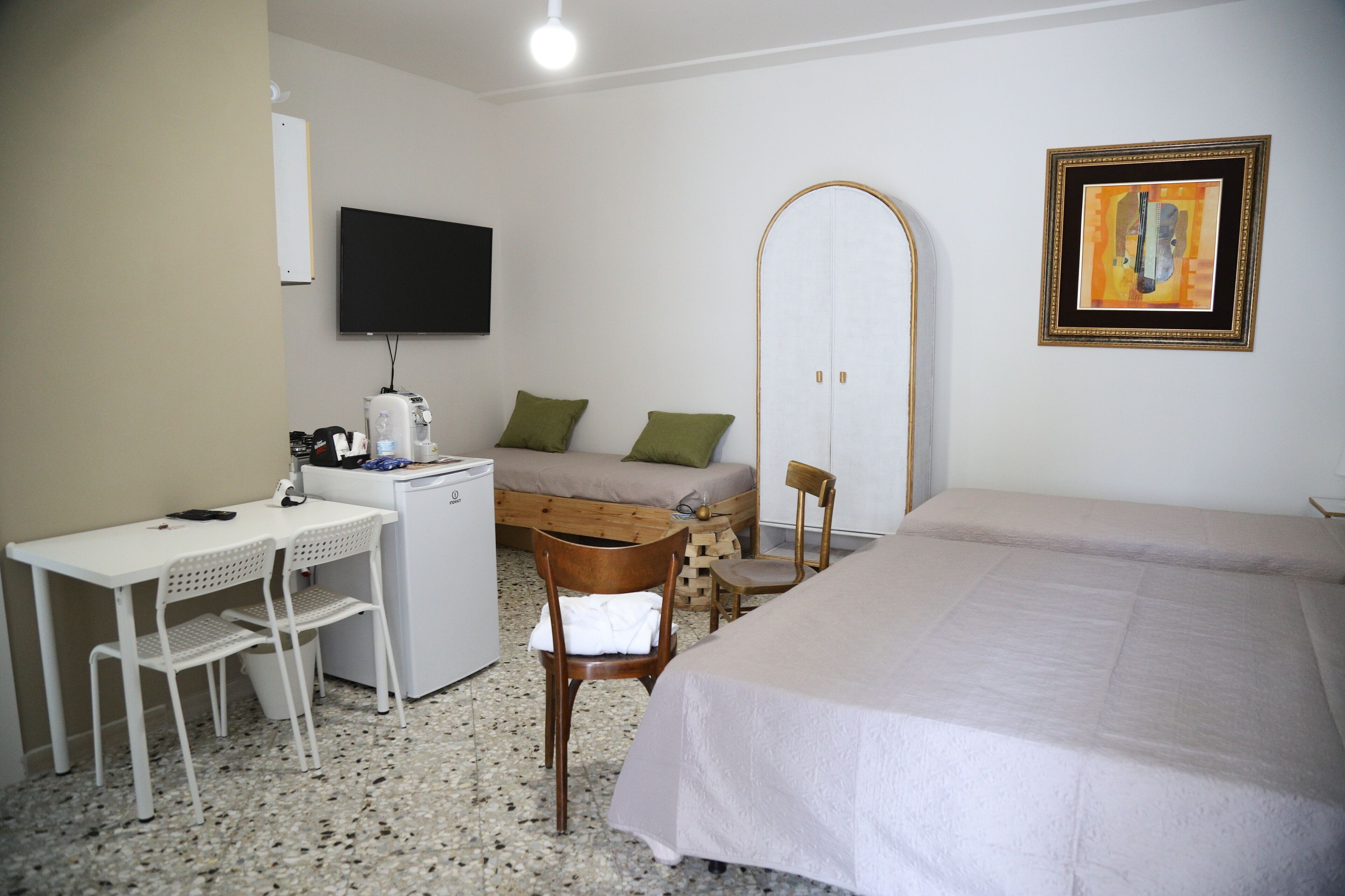 A hotel room with a bed, a desk with a chair, a small table with a chair, a wardrobe, and a television on the wall.