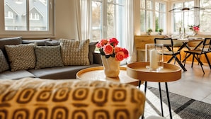 Een goed verlichte woonkamer met een bank, een bijzettafeltje met een bloevas, en een eethoek met stoelen en een tafel.