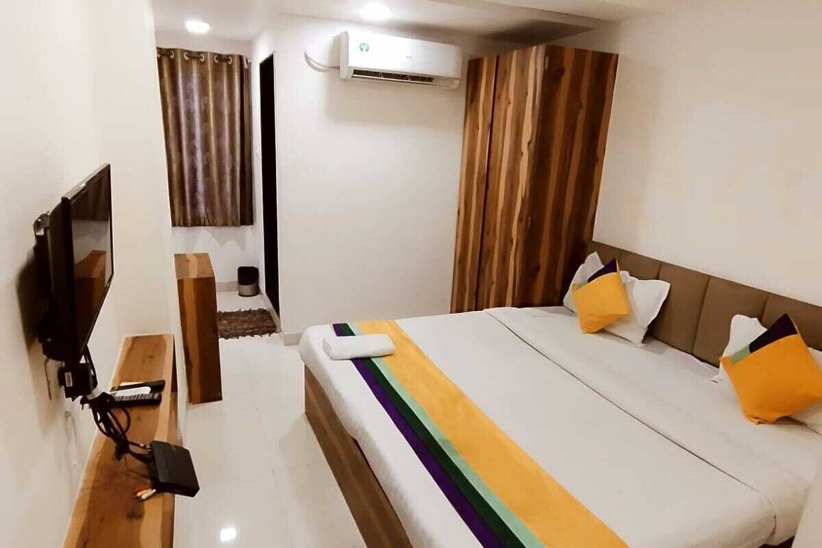 A hotel room with a bed, a TV, a wooden bench, an air conditioning unit, and a ceiling fan.