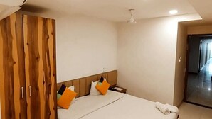 A modern bedroom with a wooden wardrobe, a bed with white bedding, and a ceiling fan. - Hotel Silvotel Stays (Indore)