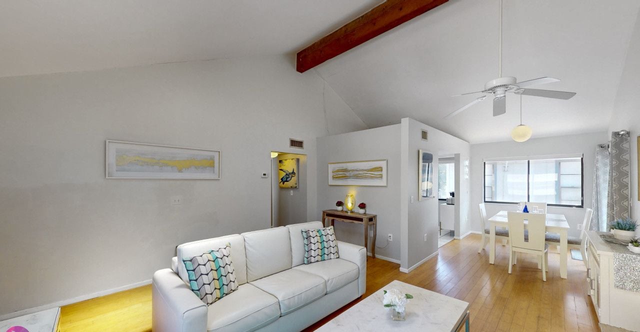 A spacious living area with a white sofa, a dining table, and a ceiling fan.
