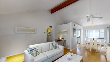 Un vaste espace de vie comprenant un canapé blanc, une table à manger et un ventilateur de plafond.