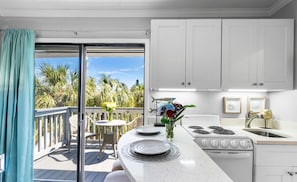 A kitchen with a large window, a dining area with a table and chairs, and a view of palm trees outside.