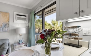 A modern kitchen with a dining area, a vase of flowers, and a view of palm trees outside.