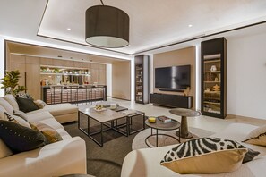 Una sala de estar moderna con sofá, mesa de centro, televisión y una cocina al fondo.