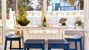 A patio area with a white fence, a table with a bottle and glass, and two blue stools. - Exclusive complex - Private Heated Pool - 100 Steps to Beach - Village 5 minute walk (Siesta Key)