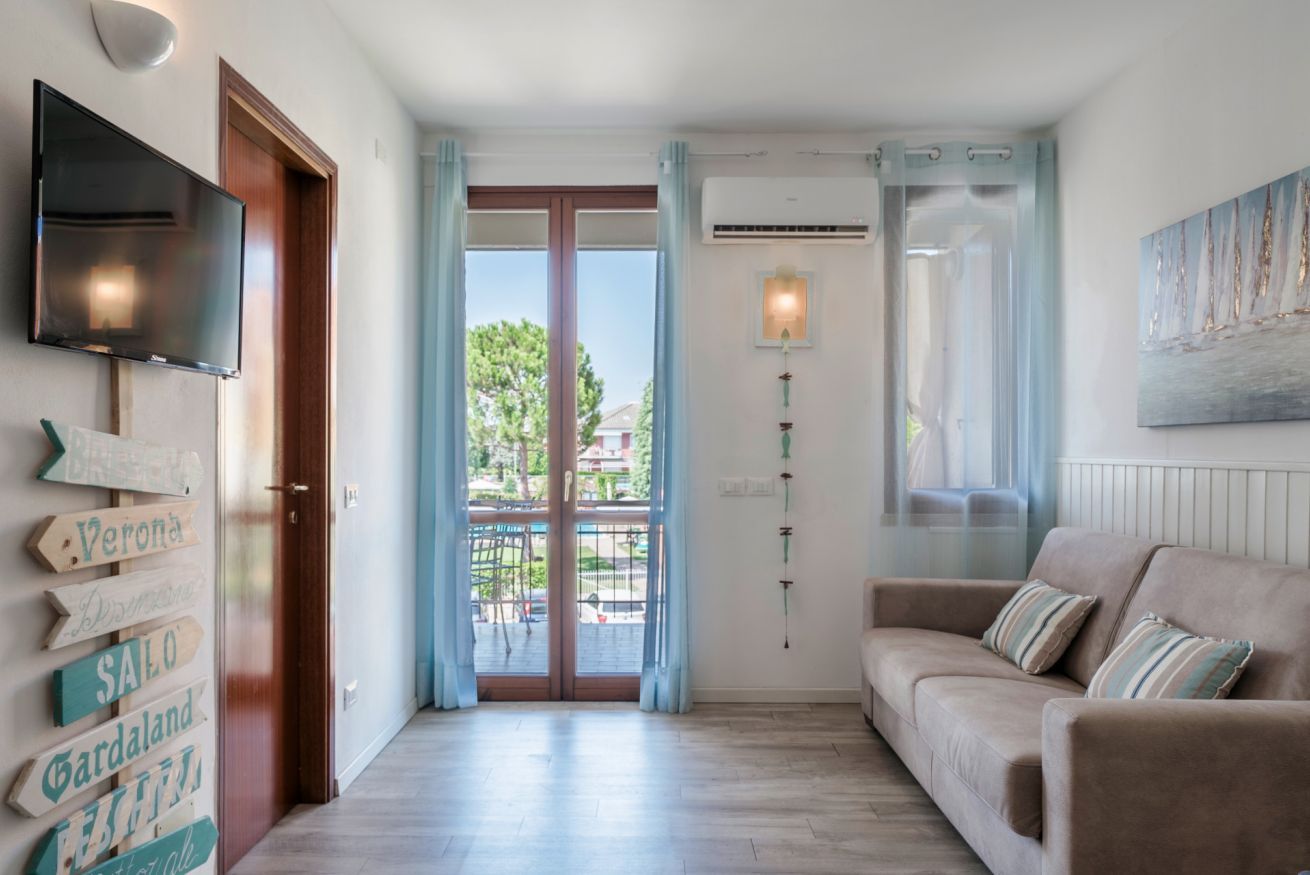 A living room with a sofa, a flat-screen TV, a wall-mounted air conditioner, and a sliding glass door leading to an outdoor area.