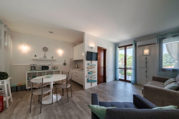 A modern living room with a sofa, a dining table with chairs, a kitchen area with a microwave, and a sliding glass door leading to an outdoor area.